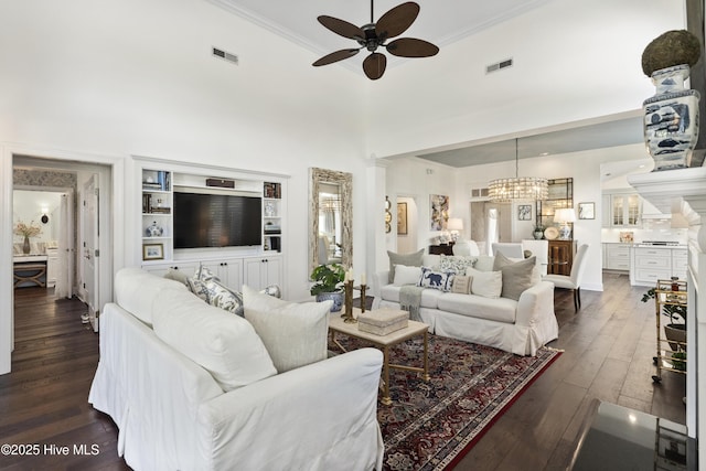 living room featuring ceiling fan, ornamental molding, dark wood finished floors, a chandelier, and a high ceiling