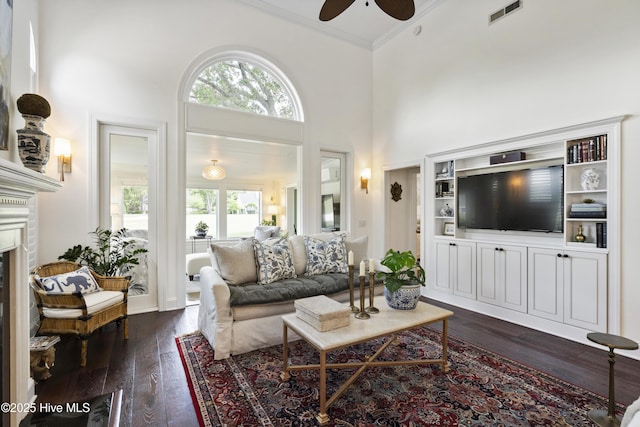 living room featuring plenty of natural light, ceiling fan, dark wood finished floors, ornamental molding, and a fireplace