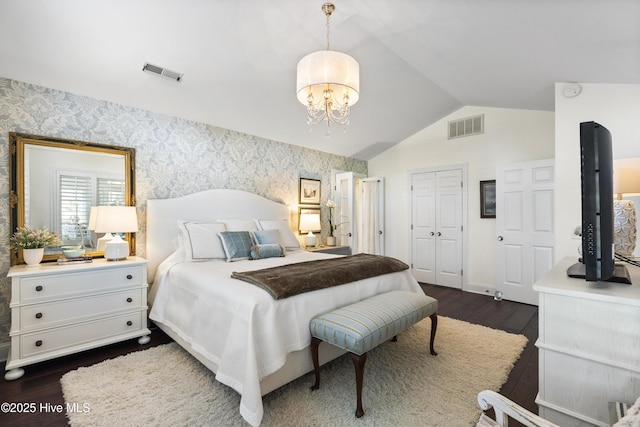 bedroom featuring dark wood finished floors, lofted ceiling, a chandelier, wallpapered walls, and a closet