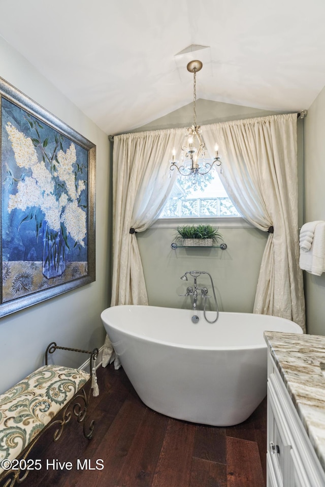 full bath with wood finished floors, a chandelier, a soaking tub, and vaulted ceiling