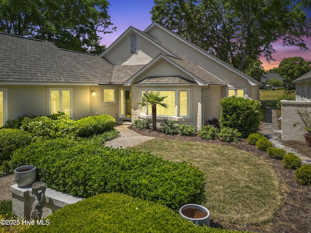view of front of home featuring stucco siding, a shingled roof, and a front lawn