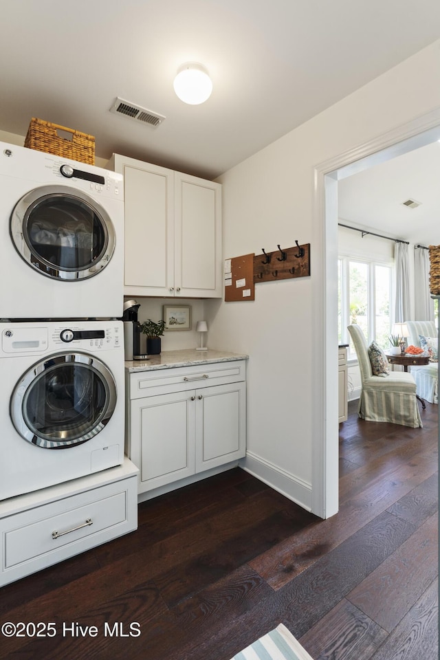 washroom with stacked washing machine and dryer, cabinet space, dark wood-style flooring, and baseboards