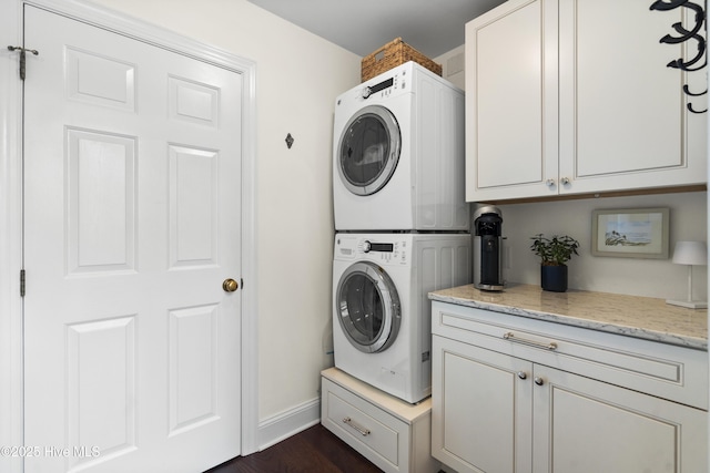 laundry room featuring stacked washer / dryer, cabinet space, baseboards, and dark wood-style flooring