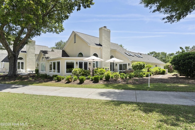 view of front of house featuring a front yard, a chimney, and stucco siding