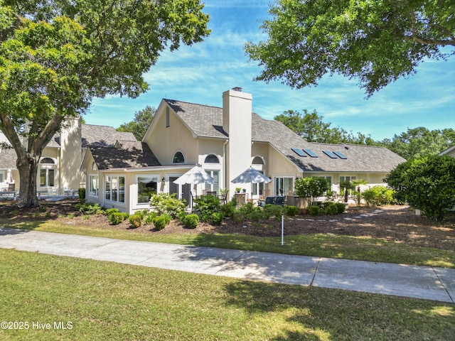 view of front of property with roof mounted solar panels, a chimney, a front yard, and stucco siding