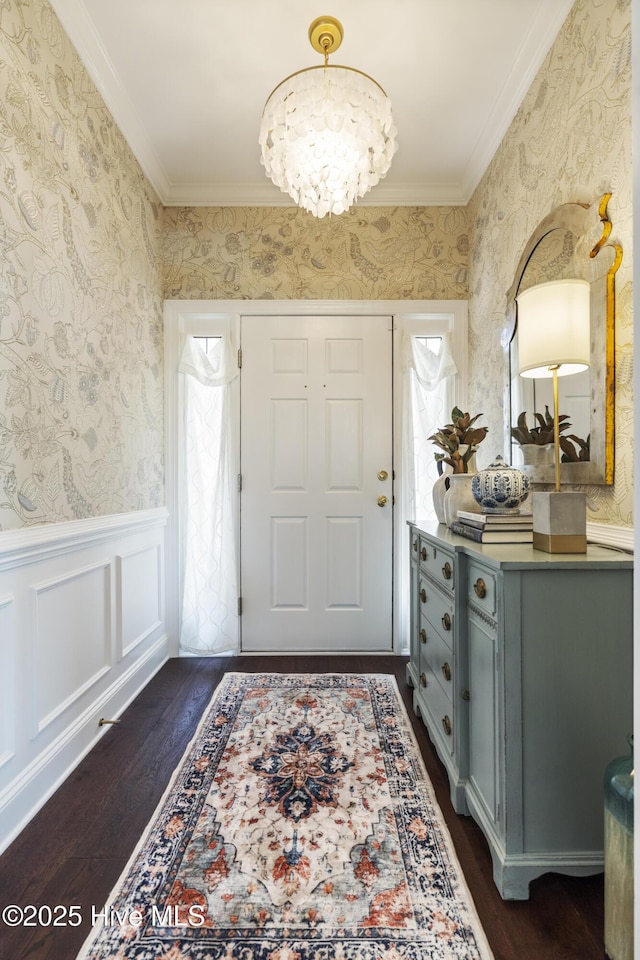 entrance foyer with wallpapered walls, dark wood-style floors, crown molding, a chandelier, and wainscoting