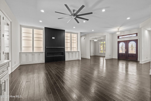 unfurnished living room featuring french doors, dark hardwood / wood-style flooring, ceiling fan with notable chandelier, and built in shelves