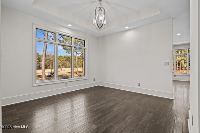 empty room featuring dark wood-type flooring, a raised ceiling, and a chandelier