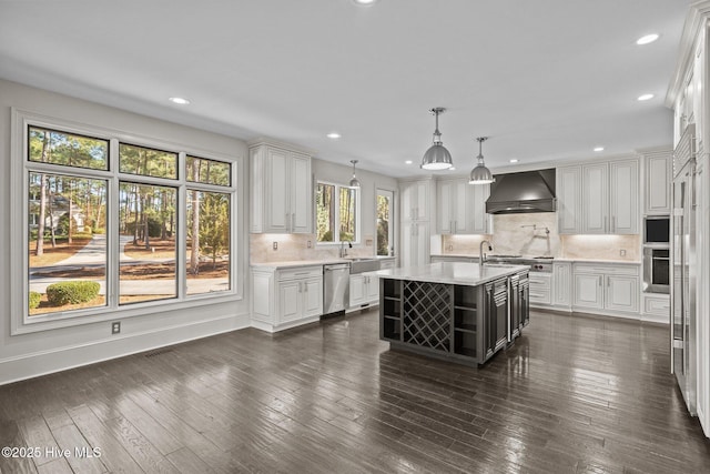 kitchen featuring hanging light fixtures, custom exhaust hood, white cabinets, and a center island with sink