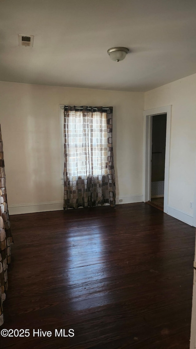 empty room featuring dark wood-style floors, visible vents, and baseboards