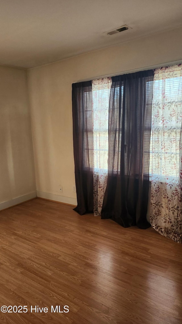 unfurnished room with wood finished floors, visible vents, and baseboards