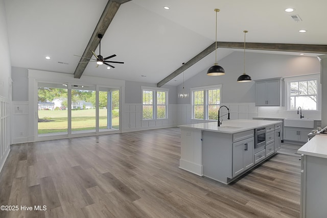 kitchen featuring gray cabinets, pendant lighting, beamed ceiling, an island with sink, and sink