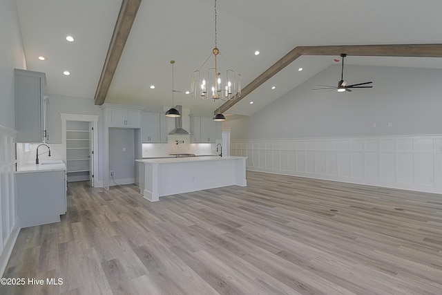 kitchen featuring pendant lighting, beamed ceiling, a center island, light hardwood / wood-style floors, and wall chimney exhaust hood