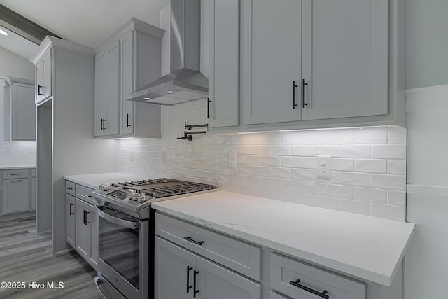 kitchen featuring gas range, light hardwood / wood-style flooring, wall chimney range hood, light stone countertops, and backsplash