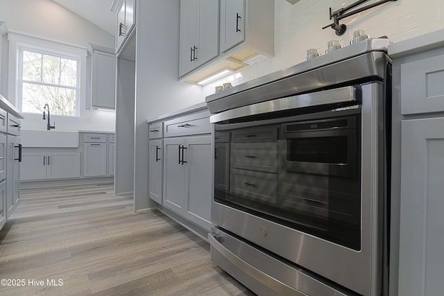 kitchen with sink, gray cabinetry, tasteful backsplash, light hardwood / wood-style floors, and vaulted ceiling