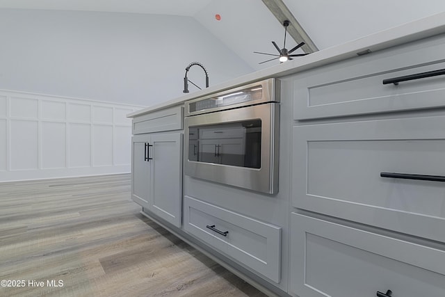 kitchen with ceiling fan, lofted ceiling, wall oven, and light wood-type flooring