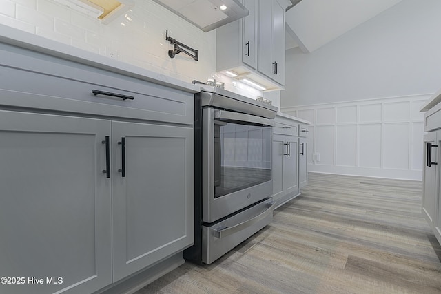 kitchen with gray cabinets, wall oven, stainless steel electric range oven, and light hardwood / wood-style floors