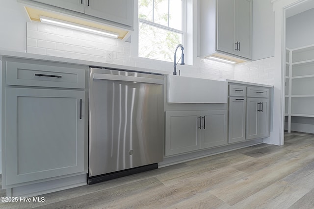 kitchen with gray cabinetry, sink, stainless steel dishwasher, and light wood-type flooring