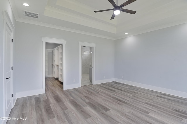 unfurnished bedroom featuring a raised ceiling, ornamental molding, ensuite bathroom, and light wood-type flooring