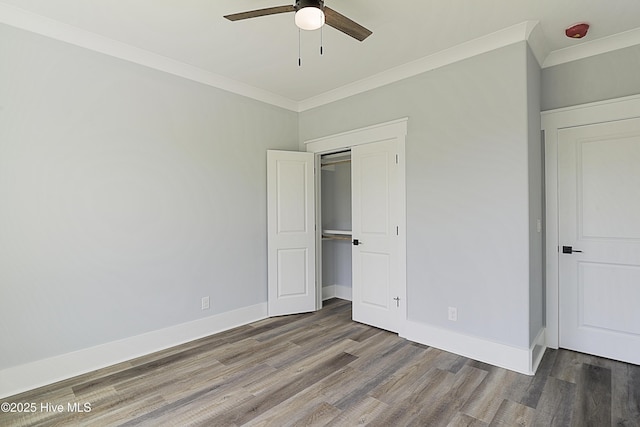 unfurnished bedroom featuring crown molding, dark wood-type flooring, ceiling fan, and a closet