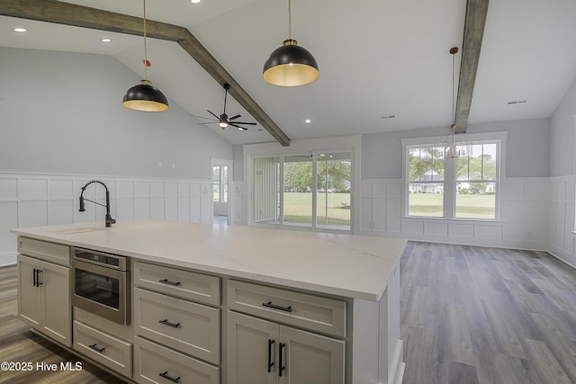 kitchen with sink, hanging light fixtures, light hardwood / wood-style flooring, an island with sink, and light stone countertops