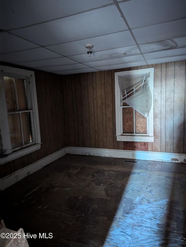 unfurnished room featuring a drop ceiling and wood walls