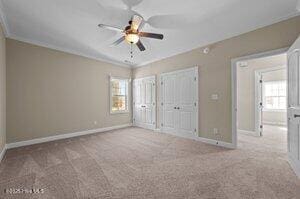 unfurnished bedroom featuring ornamental molding, carpet flooring, two closets, and baseboards