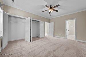 unfurnished bedroom with ensuite bathroom, carpet flooring, a ceiling fan, baseboards, and ornamental molding