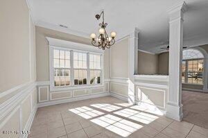 unfurnished dining area with decorative columns, ornamental molding, tile patterned flooring, a chandelier, and a decorative wall