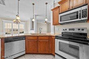 kitchen featuring a peninsula, a sink, appliances with stainless steel finishes, brown cabinets, and decorative light fixtures