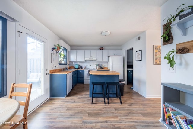 kitchen featuring a breakfast bar, white cabinetry, butcher block counters, white appliances, and light wood-type flooring