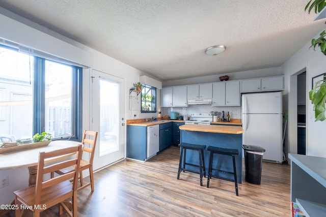 kitchen with blue cabinetry, white appliances, wood counters, and light hardwood / wood-style flooring