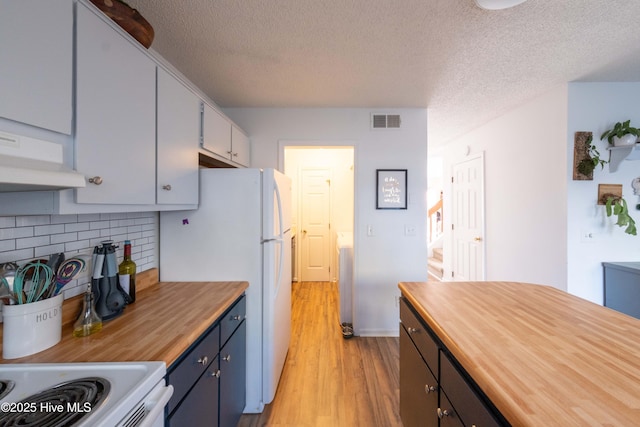 kitchen featuring butcher block countertops, decorative backsplash, white fridge, light hardwood / wood-style floors, and a textured ceiling