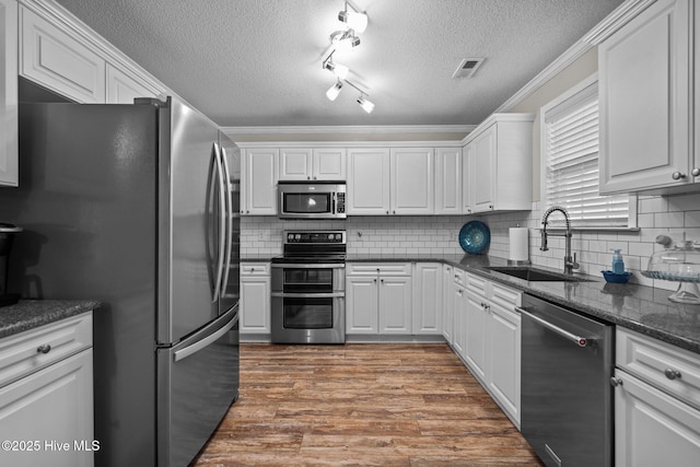 kitchen featuring sink, white cabinetry, hardwood / wood-style floors, stainless steel appliances, and decorative backsplash