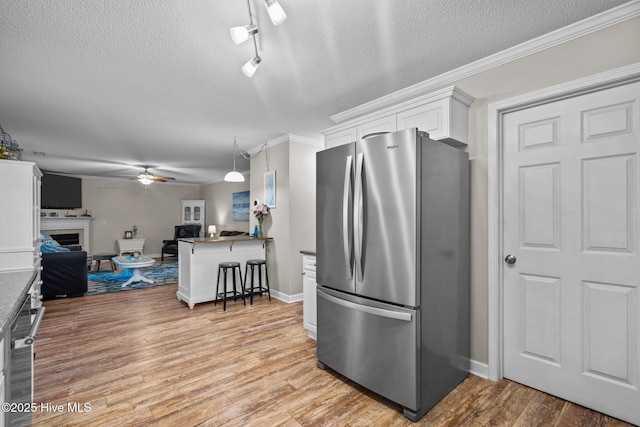 kitchen featuring a kitchen bar, light wood-type flooring, white cabinets, kitchen peninsula, and stainless steel refrigerator