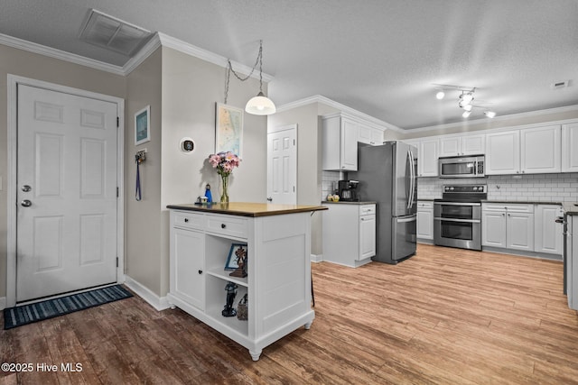 kitchen with appliances with stainless steel finishes, white cabinets, hanging light fixtures, and light hardwood / wood-style floors