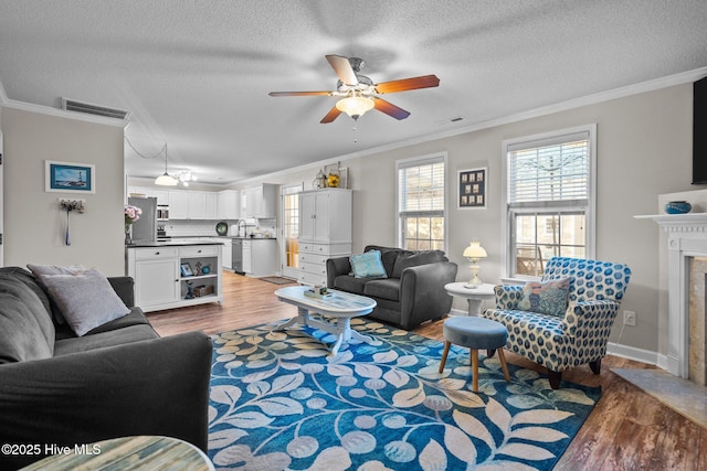 living room featuring a fireplace, hardwood / wood-style flooring, ornamental molding, ceiling fan, and a textured ceiling