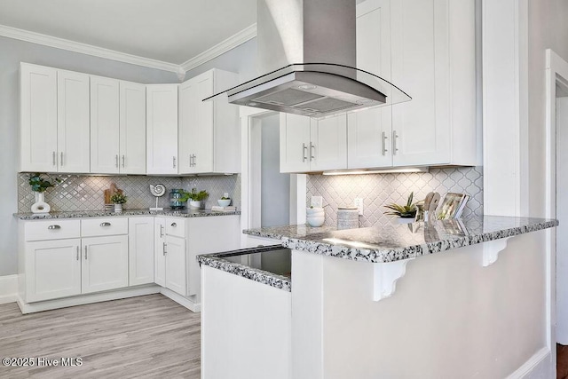 kitchen with a breakfast bar area, white cabinetry, ornamental molding, stone counters, and island exhaust hood