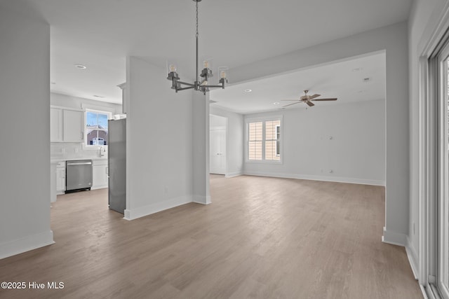 unfurnished living room with a healthy amount of sunlight, ceiling fan with notable chandelier, and light hardwood / wood-style flooring