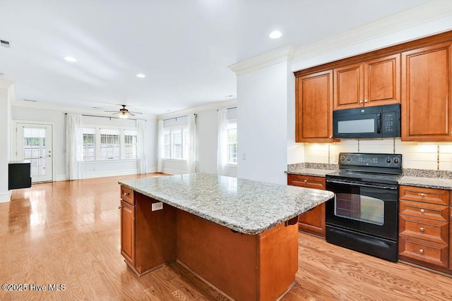 kitchen with light hardwood / wood-style floors, plenty of natural light, black appliances, and a center island