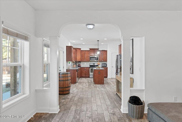 kitchen with hanging light fixtures, stainless steel appliances, ornate columns, and a kitchen island