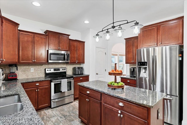 kitchen with a kitchen island, tasteful backsplash, dark stone countertops, hanging light fixtures, and stainless steel appliances