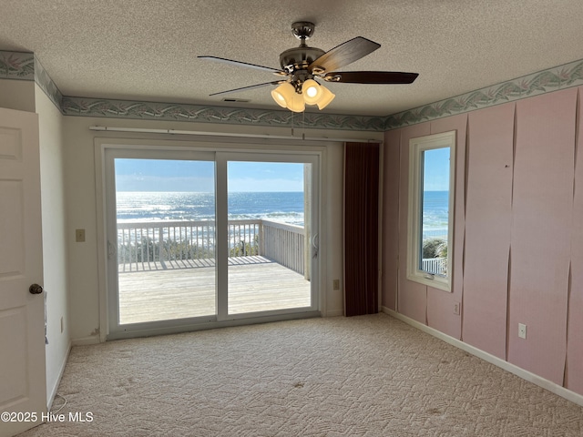 empty room with ceiling fan, light colored carpet, a textured ceiling, and a water view