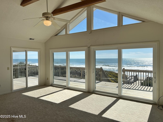 unfurnished sunroom featuring vaulted ceiling with beams, ceiling fan, a beach view, and a water view