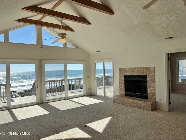 unfurnished living room with a view of the beach, beamed ceiling, carpet flooring, ceiling fan, and a water view