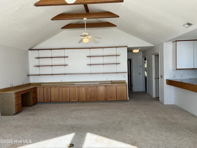 kitchen featuring vaulted ceiling with beams, built in desk, light colored carpet, and a textured ceiling