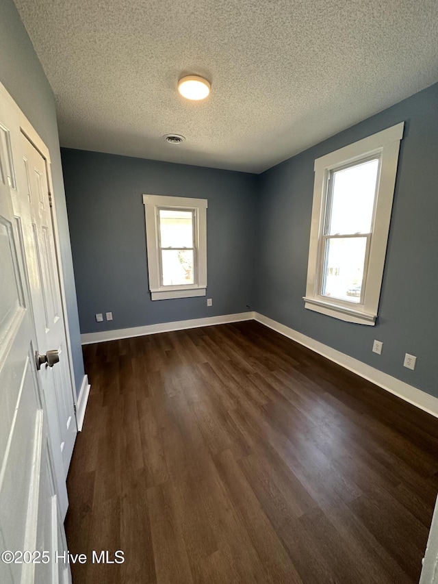 unfurnished bedroom with dark wood finished floors, a textured ceiling, and baseboards