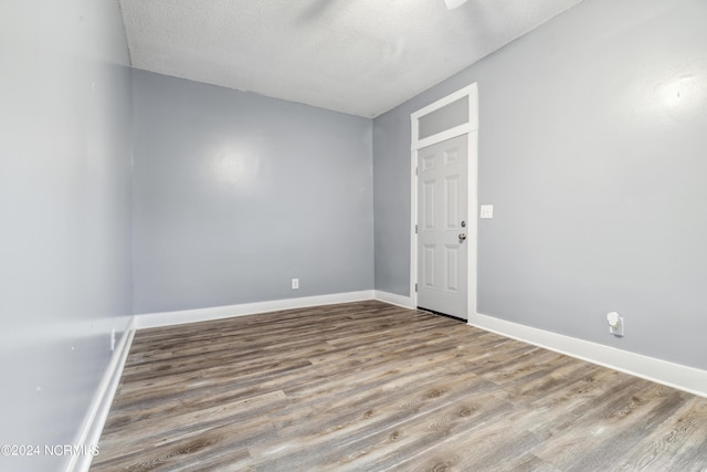 spare room with a textured ceiling, wood finished floors, and baseboards