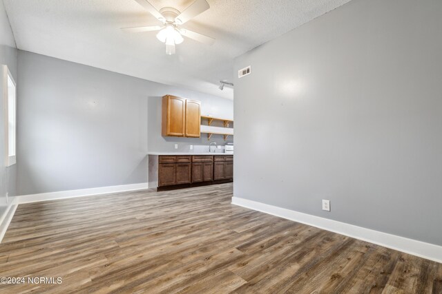 unfurnished living room with baseboards, a textured ceiling, a ceiling fan, and wood finished floors