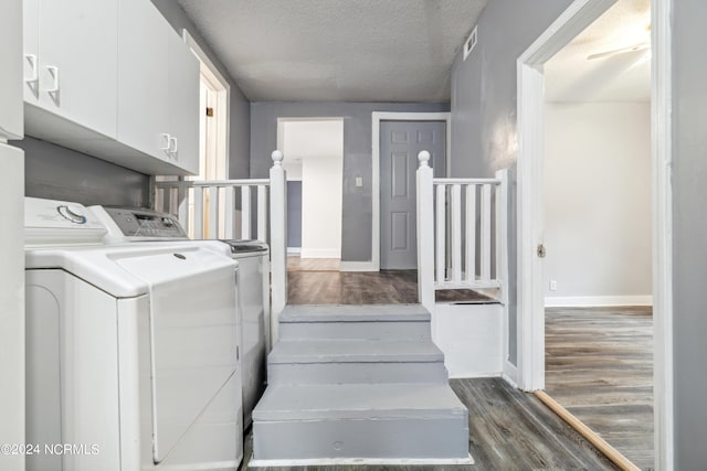 laundry area with a textured ceiling, washing machine and dryer, wood finished floors, visible vents, and cabinet space